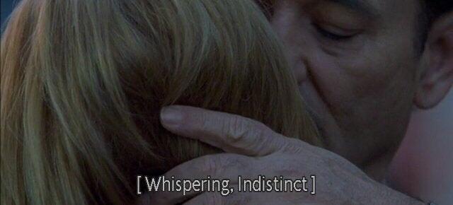 Close-up screenshot from Lost in Translation showing a man whispering into a blonde woman’s ear during an intimate goodbye embrace, with the subtitle '[Whispering, Indistinct]' at the bottom.